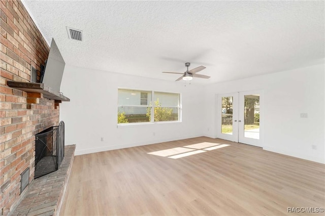 unfurnished living room with a brick fireplace, light hardwood / wood-style flooring, french doors, and a textured ceiling