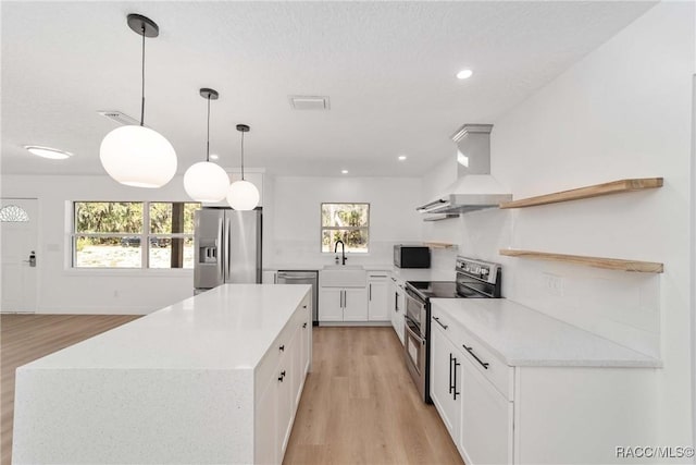 kitchen featuring white cabinetry, sink, hanging light fixtures, stainless steel appliances, and wall chimney range hood