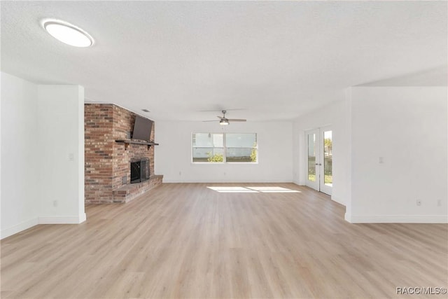 unfurnished living room with light hardwood / wood-style flooring, a textured ceiling, a brick fireplace, and a wealth of natural light