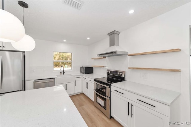 kitchen with white cabinetry, stainless steel appliances, decorative light fixtures, wall chimney exhaust hood, and light wood-type flooring