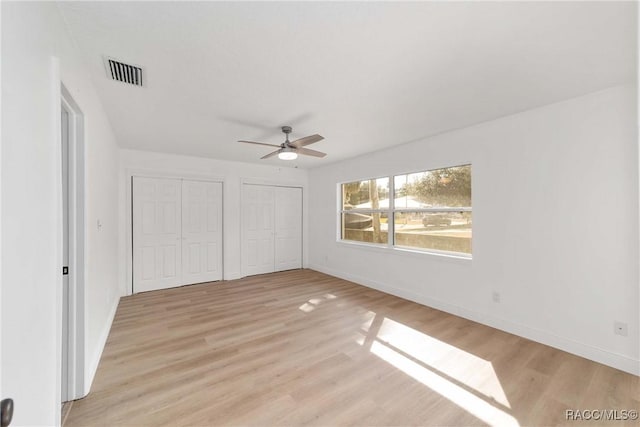 unfurnished bedroom with ceiling fan, two closets, and light wood-type flooring