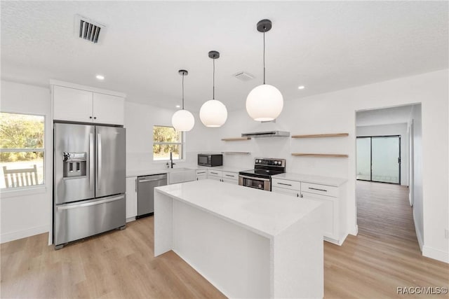 kitchen featuring light hardwood / wood-style flooring, appliances with stainless steel finishes, white cabinetry, a center island, and decorative light fixtures