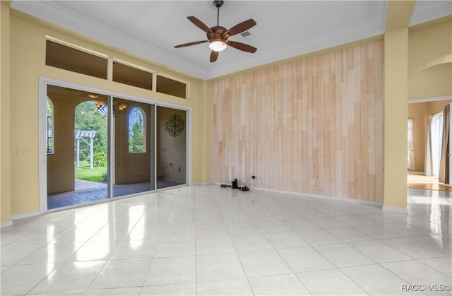 unfurnished room featuring light tile patterned flooring, ceiling fan, ornamental molding, and wood walls