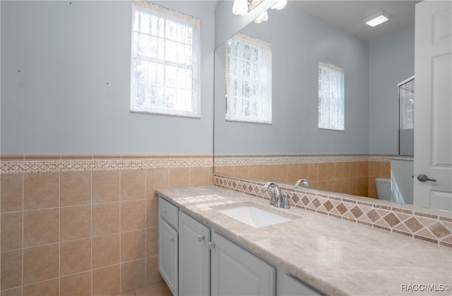 bathroom with vanity, toilet, plenty of natural light, and tile walls