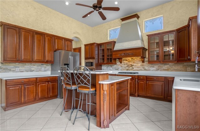 kitchen featuring ceiling fan, a kitchen island, light tile patterned floors, custom range hood, and appliances with stainless steel finishes