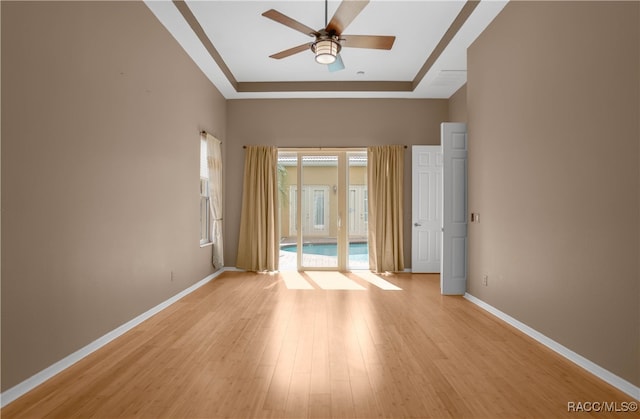 empty room featuring light wood-type flooring, a tray ceiling, and ceiling fan