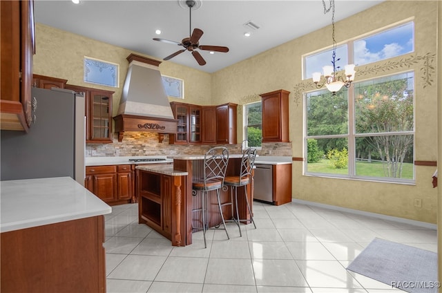 kitchen with a kitchen breakfast bar, premium range hood, ceiling fan with notable chandelier, stainless steel appliances, and a kitchen island