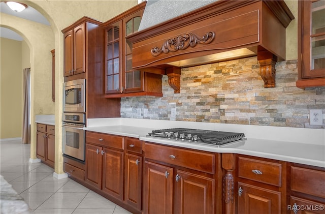 kitchen with tasteful backsplash, light tile patterned flooring, premium range hood, and appliances with stainless steel finishes