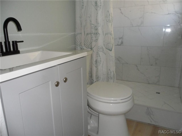 bathroom with toilet, wood finished floors, tiled shower, and vanity