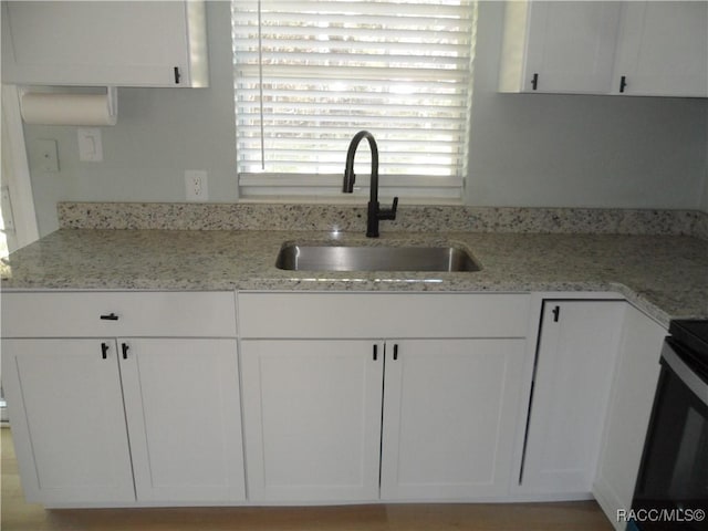 kitchen featuring light stone counters, a sink, and white cabinetry