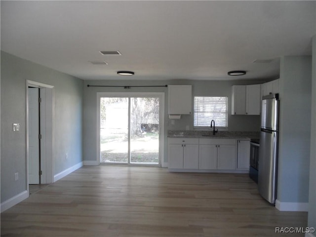 kitchen featuring light wood finished floors, white cabinets, a sink, and freestanding refrigerator