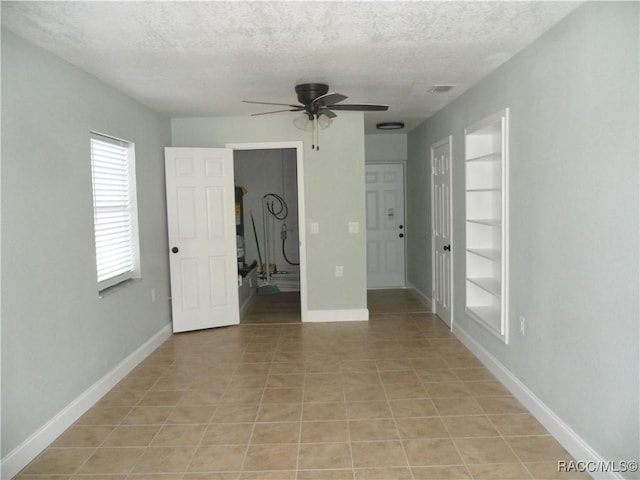 spare room with a textured ceiling, ceiling fan, light tile patterned floors, baseboards, and built in features