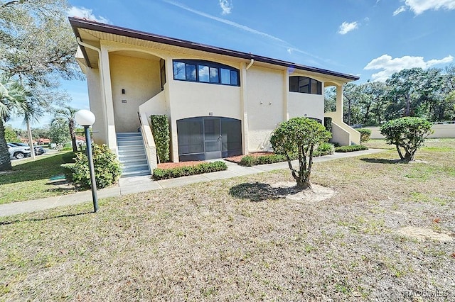 view of front facade with stucco siding, a front lawn, and stairs