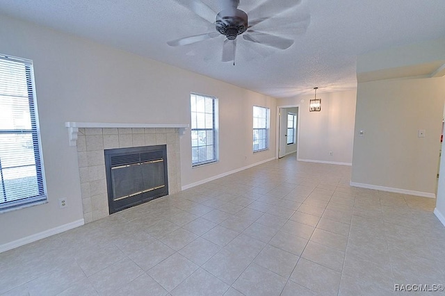 unfurnished living room featuring ceiling fan, a tiled fireplace, a textured ceiling, and light tile patterned floors