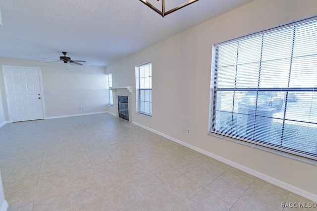 unfurnished living room with a tiled fireplace, light tile patterned floors, a textured ceiling, and ceiling fan