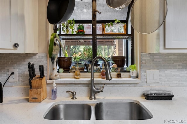 details with tasteful backsplash, light stone counters, sink, and white cabinets