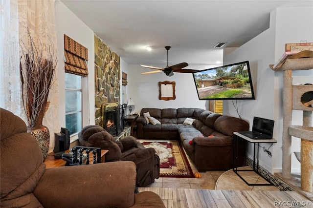 tiled living room with ceiling fan and a fireplace