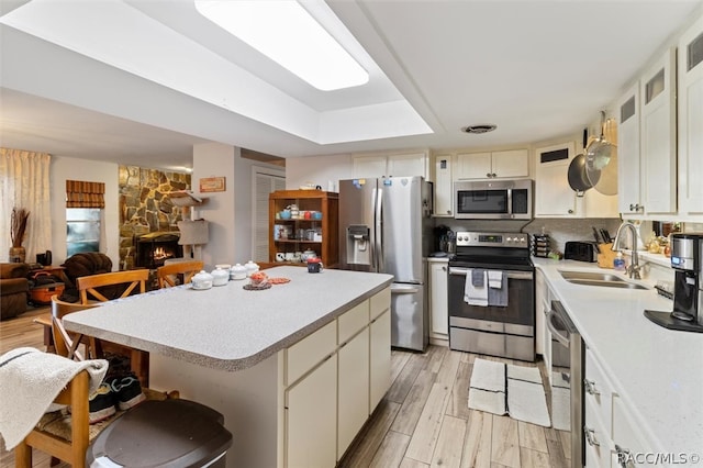 kitchen with sink, light hardwood / wood-style flooring, a fireplace, appliances with stainless steel finishes, and a kitchen island