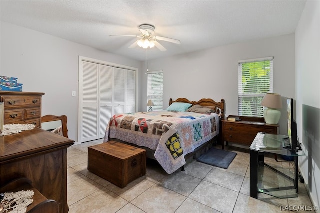 bedroom with light tile patterned floors, a textured ceiling, a closet, and ceiling fan