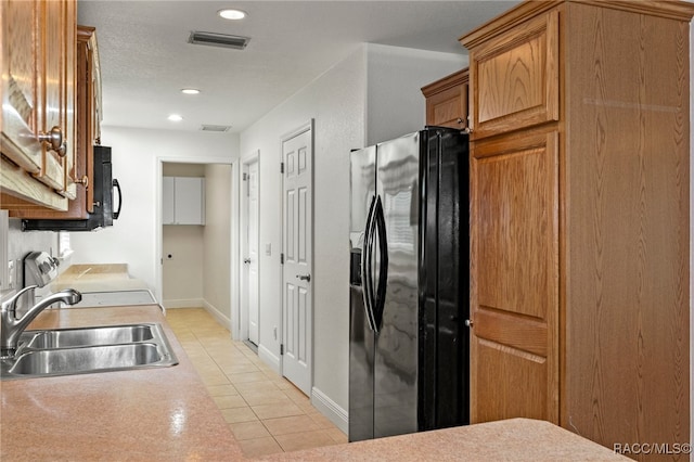 kitchen featuring light tile patterned floors, sink, stove, and black fridge