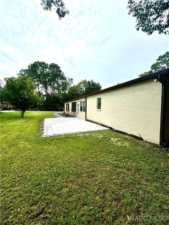 back of property featuring a patio, a lawn, and stucco siding