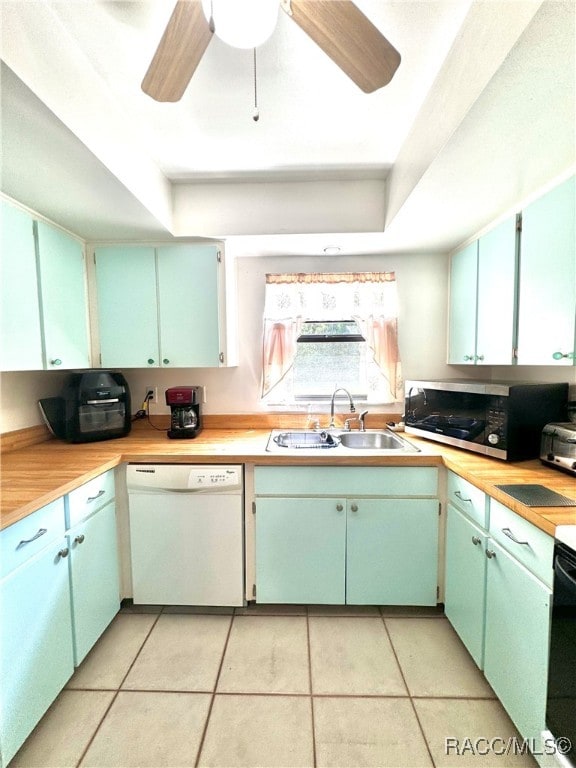 kitchen with stainless steel microwave, white dishwasher, a tray ceiling, light countertops, and a sink