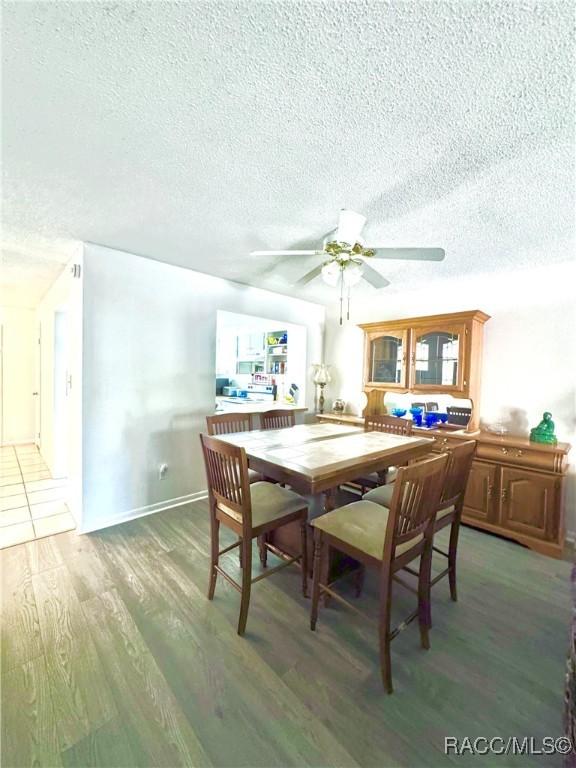 dining space featuring ceiling fan, a textured ceiling, baseboards, and wood finished floors