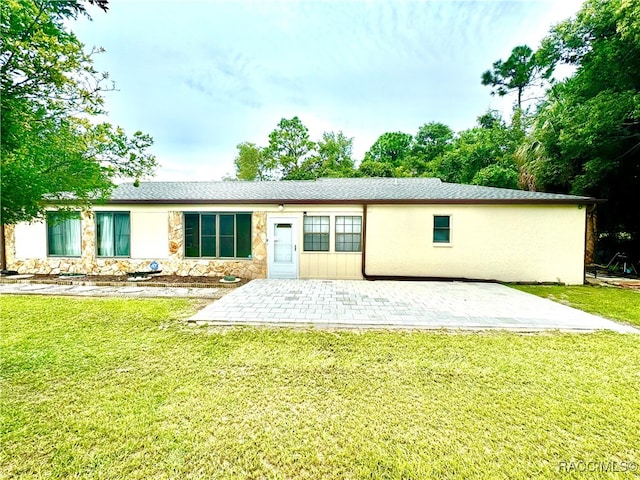 rear view of property featuring stone siding, stucco siding, a lawn, and a patio