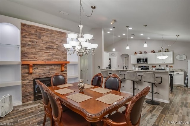 dining space with dark hardwood / wood-style floors, an inviting chandelier, a stone fireplace, and vaulted ceiling