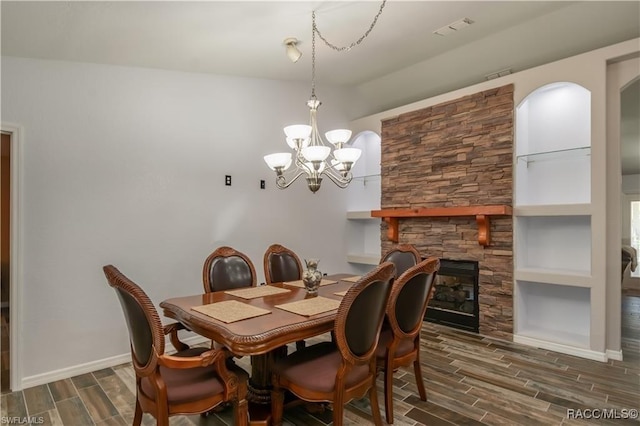 dining space featuring a notable chandelier, a stone fireplace, dark hardwood / wood-style flooring, and built in features