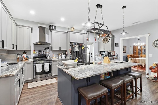 kitchen with a breakfast bar, decorative light fixtures, a kitchen island, stainless steel appliances, and wall chimney range hood