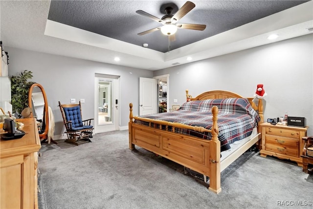 bedroom with ceiling fan, a raised ceiling, a textured ceiling, and dark colored carpet