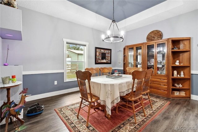 dining area with an inviting chandelier, a tray ceiling, and dark wood-type flooring