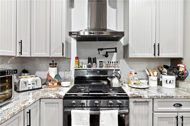 kitchen with gas range, wall chimney exhaust hood, light stone countertops, and white cabinets