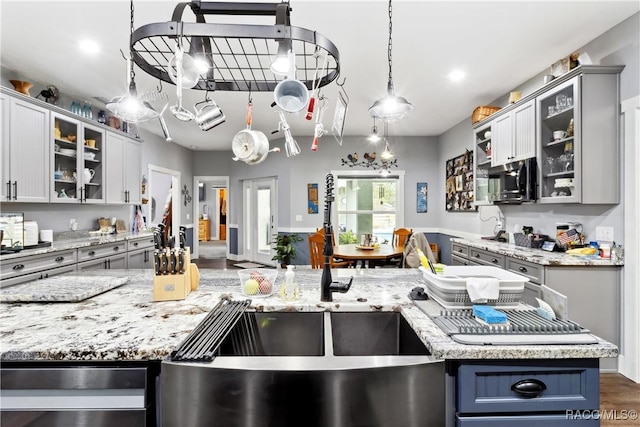 kitchen with hanging light fixtures, light stone countertops, dark wood-type flooring, and gray cabinetry