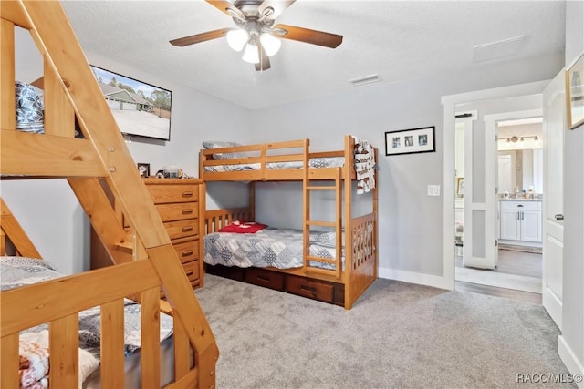 bedroom with a textured ceiling, connected bathroom, light colored carpet, and ceiling fan