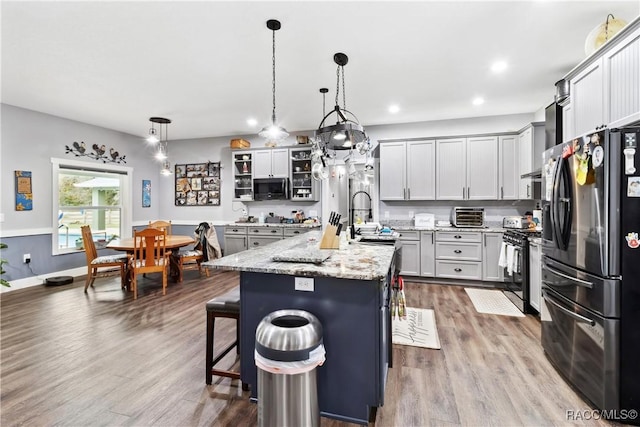 kitchen with a breakfast bar area, decorative light fixtures, stainless steel appliances, light stone countertops, and a kitchen island with sink