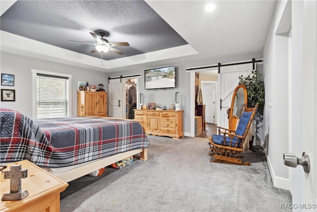 carpeted bedroom with a barn door, a textured ceiling, ceiling fan, and a tray ceiling