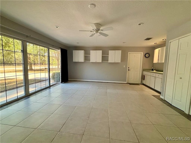 unfurnished living room featuring a textured ceiling, ceiling fan, light tile patterned floors, and sink