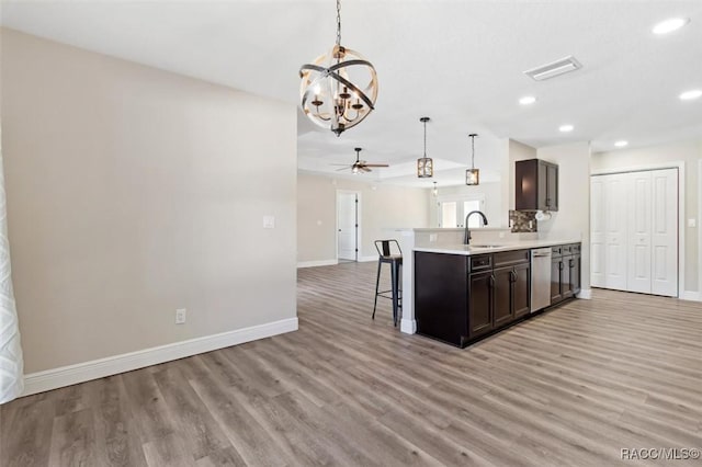 kitchen with dark brown cabinetry, sink, decorative light fixtures, stainless steel dishwasher, and a kitchen breakfast bar