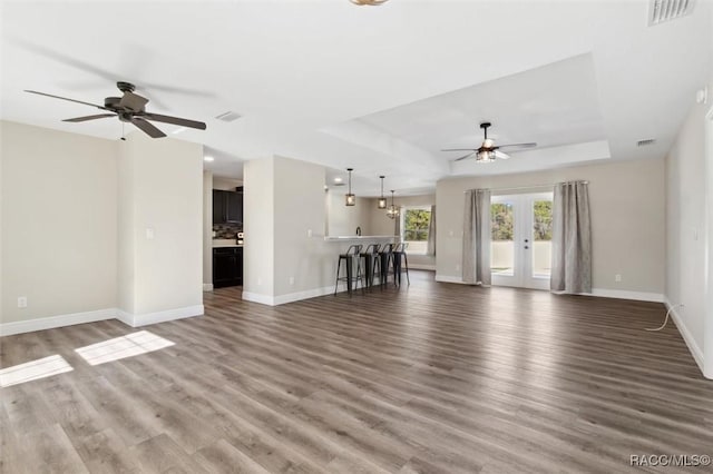 unfurnished living room with a tray ceiling, wood-type flooring, french doors, and ceiling fan