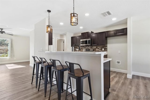 kitchen with light hardwood / wood-style flooring, a breakfast bar area, hanging light fixtures, tasteful backsplash, and kitchen peninsula