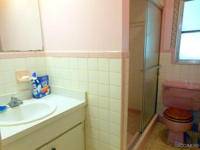 bathroom featuring tile walls, a shower stall, vanity, toilet, and wainscoting
