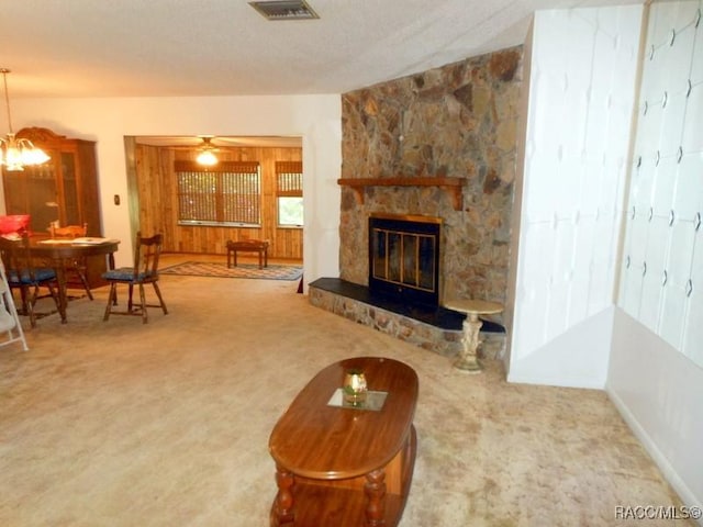 living area featuring an inviting chandelier, carpet, visible vents, and a stone fireplace