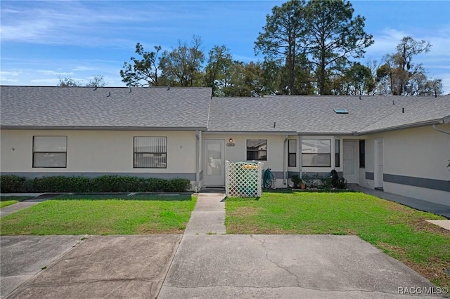 view of front of property with a shingled roof, a front lawn, and stucco siding