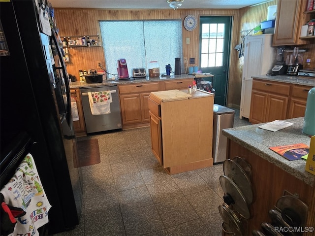 kitchen with black fridge, dishwasher, a kitchen island, and wood walls