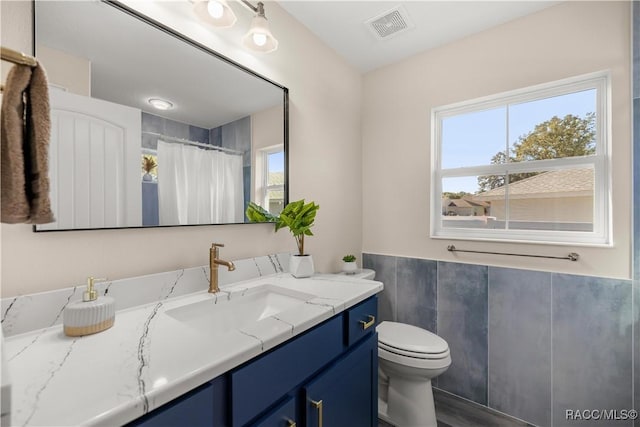 bathroom with toilet, a shower with shower curtain, a healthy amount of sunlight, and vanity