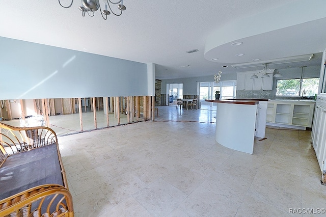 kitchen featuring decorative backsplash, a textured ceiling, sink, an inviting chandelier, and white cabinetry