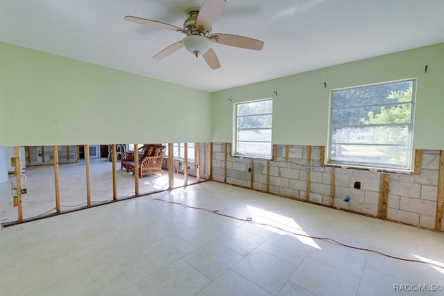 tiled empty room featuring a wealth of natural light, ceiling fan, and tile walls