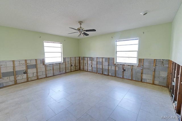 tiled empty room with a textured ceiling, ceiling fan, and tile walls